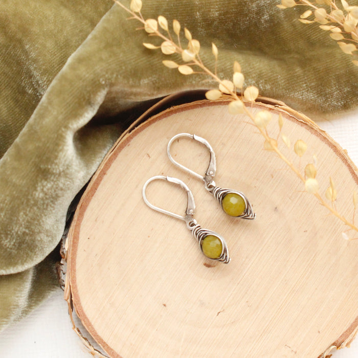 The olivine jade wrapped earrings styled on wood with green velvet and dried grass