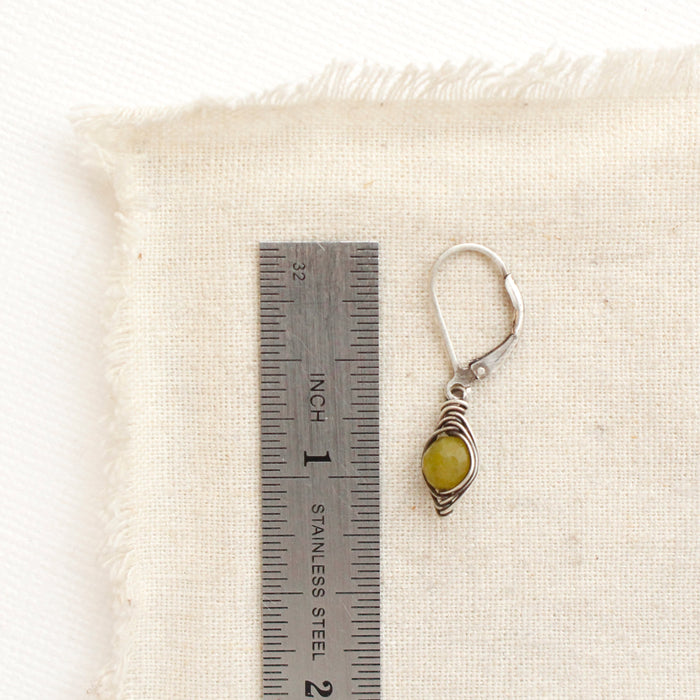 A olivine jade wrapped earring next to a ruler for size reference