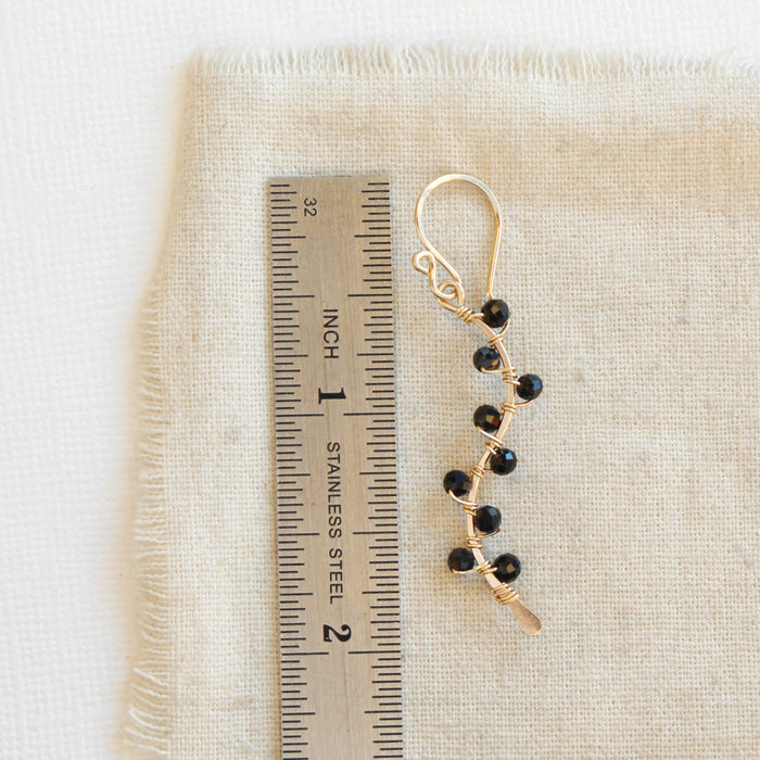 A onyx wrapped gold vine earring next to a ruler for size reference