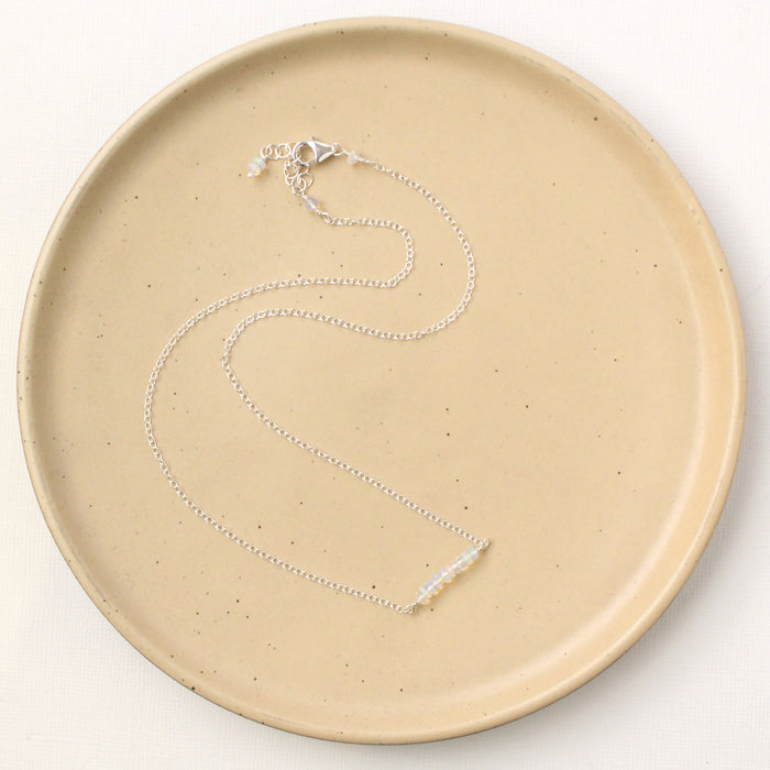 The opal bar necklace styled on a tan plate to show the adjustable lobster clasp closure