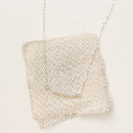 The opal bar necklace styled on tan linen