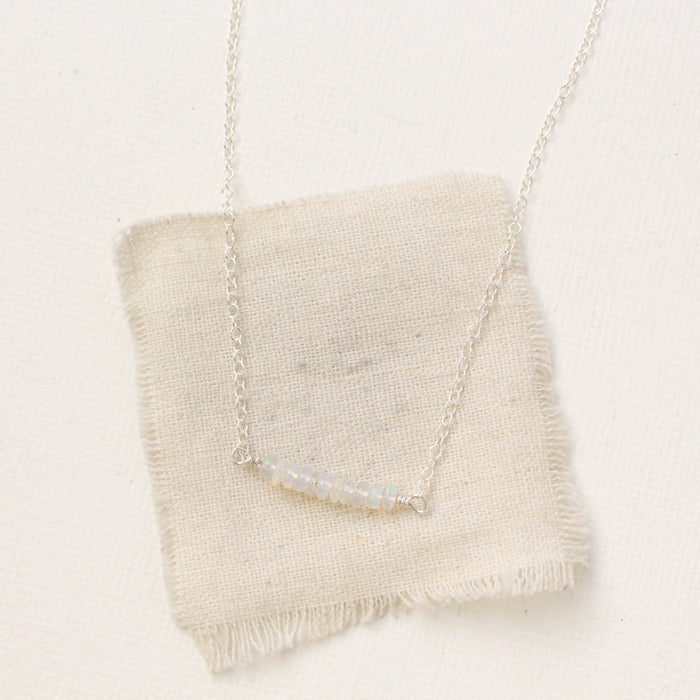 The opal bar necklace styled on tan linen