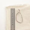 An organic silver hoop earring next to a ruler for size reference