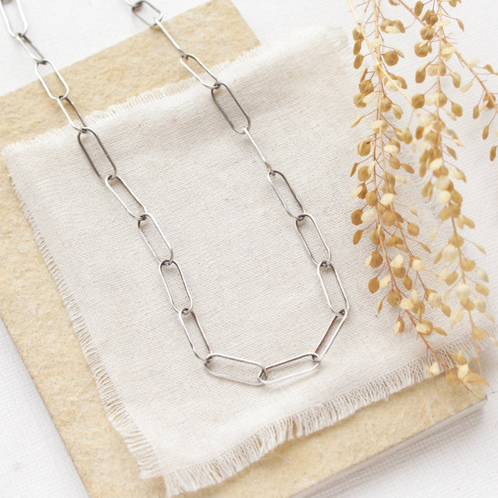 The oxidized silver paperclip necklace styled on a tan rock with linen and dried grass