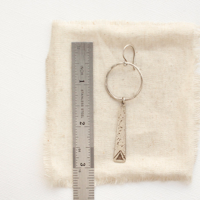A pakal long triangle hoop earring next to a ruler for size reference