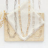 All three paperclip chain necklaces styled on a tan rock with linen and dried grass