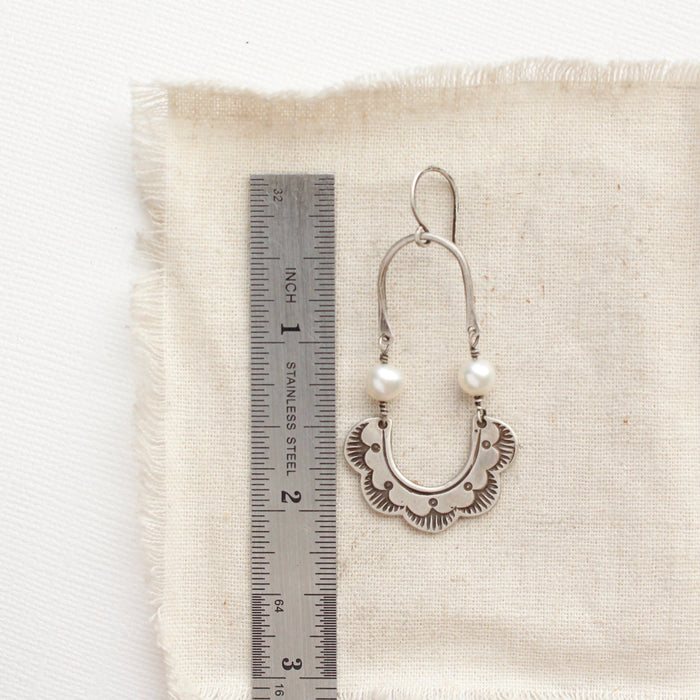 A pearl columbine hoop earring next to a ruler for size reference
