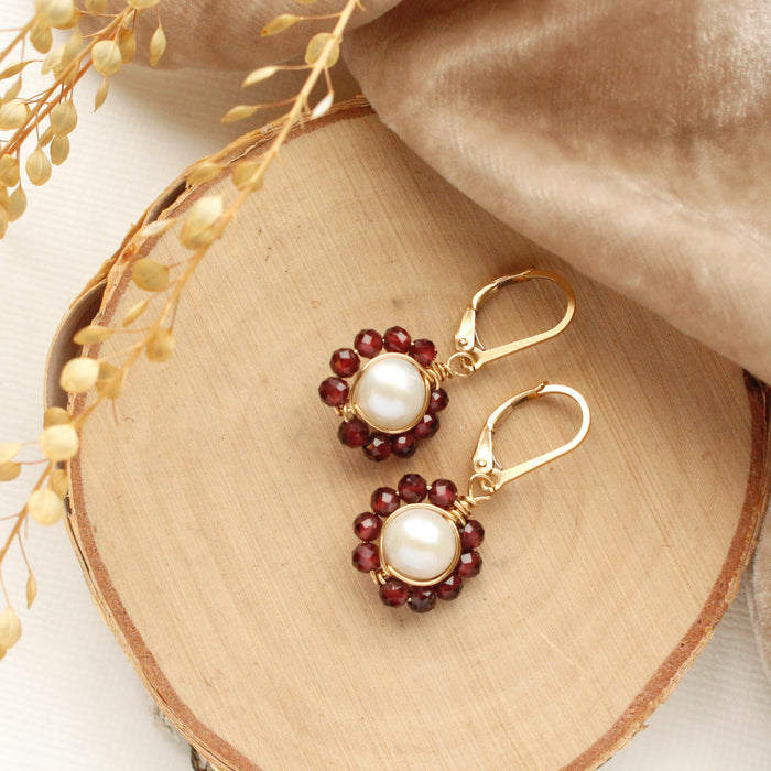 The pearl and garnet flower earrings styled on wood with brown velvet and dried grass