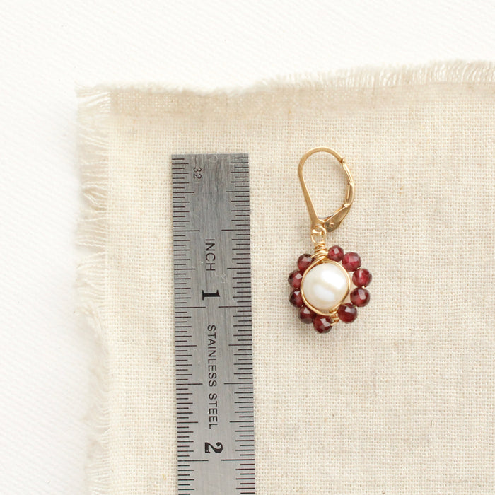 A pearl and garnet flower earring next to a ruler for size reference