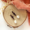 The pearl and leather earrings styled on wood with orange velvet and dried grass