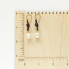 The pearl and leather earrings on a wooden ruler for size reference