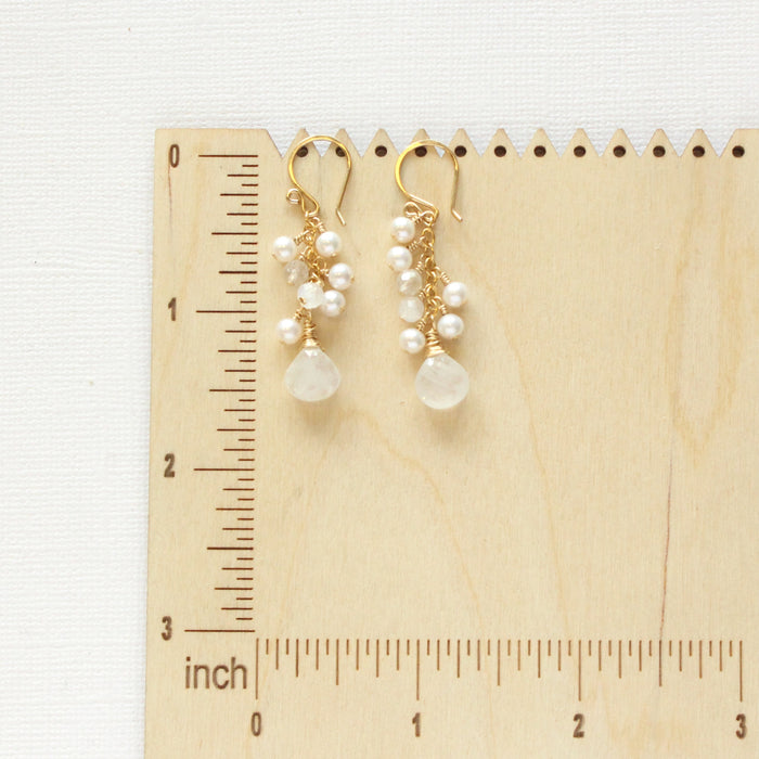 The pearl and moonstone fringe earrings on a wooden ruler for size reference