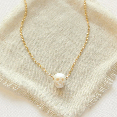 The carved pearl skull necklace styled on tan linen