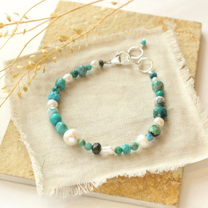 The pearl and turquoise bracelet styled on a tan rock with dried grass