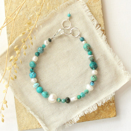 The mixed turquoise and pearl bracelet styled on a tan rock with linen and dried grass