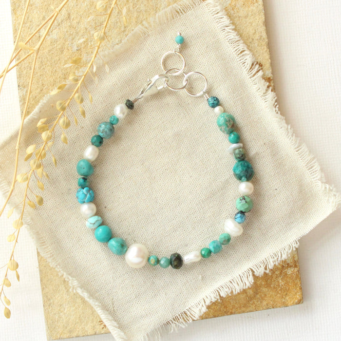 The mixed turquoise and pearl bracelet styled on a tan rock with linen and dried grass