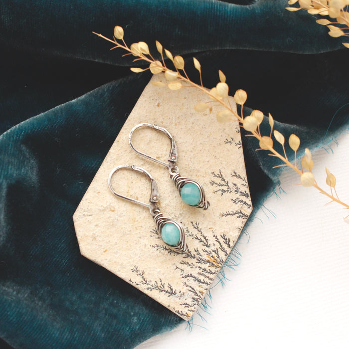 The wrapped amazonite earrings styled on a tan rock with blue velvet and dried grass