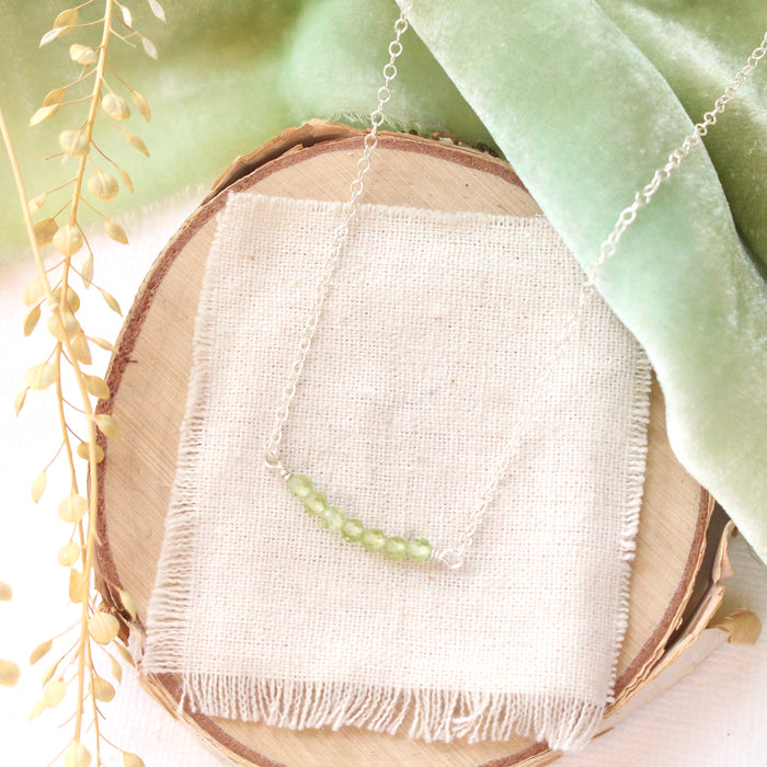 The peridot bar necklace styled on wood with green velvet and dried grass