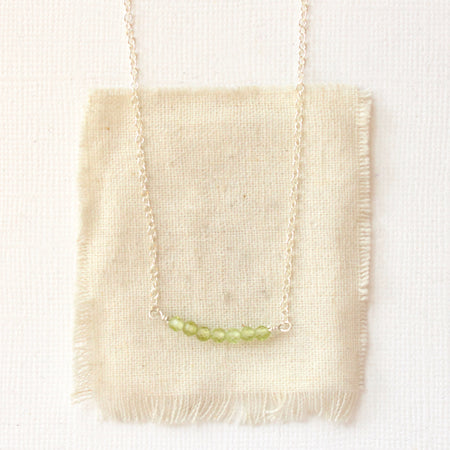 The peridot bar necklace styled on tan linen