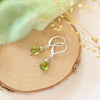 The peridot drop earrings styled on wood with green velvet and dried grass