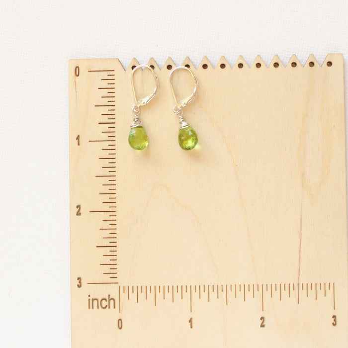 The peridot drop earrings on a wooden ruler for size reference