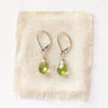 The peridot drop earrings styled on tan linen