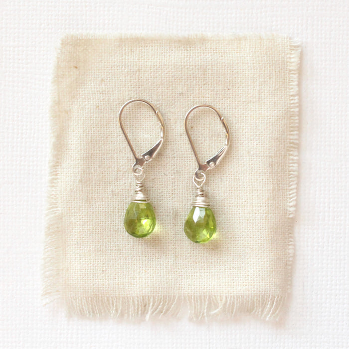 The peridot drop earrings styled on tan linen