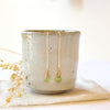 The peridot drop hook earrings styled on a ceramic cup with dried grass