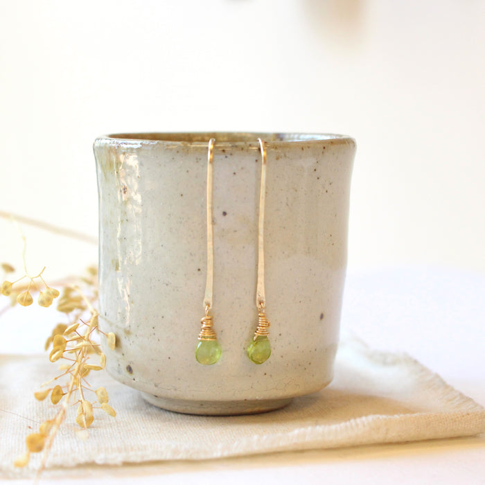 The peridot drop hook earrings styled on a ceramic cup with dried grass