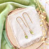 The peridot drop hook earrings styled on wood with green velvet and dried grass