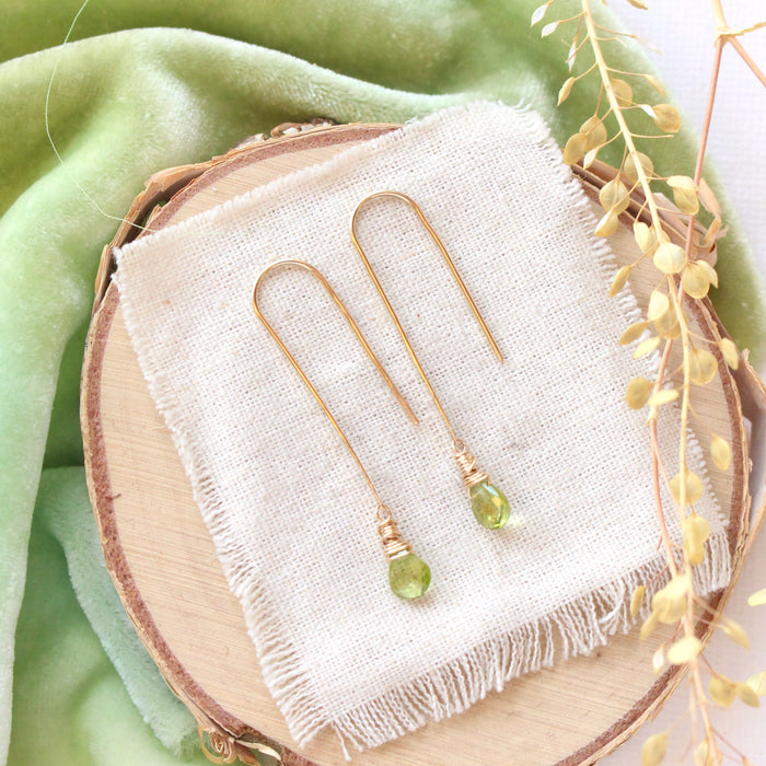 The peridot drop hook earrings styled on wood with green velvet and dried grass