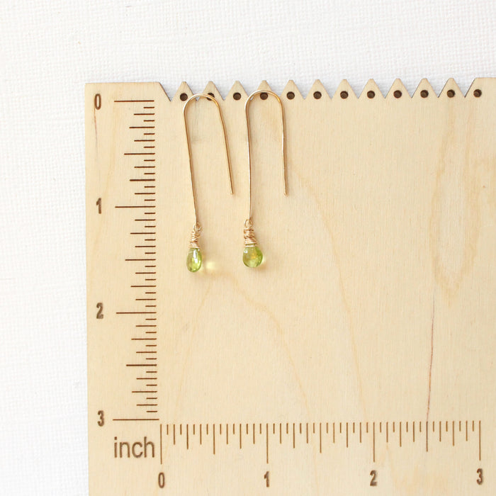 The peridot drop hook earrings on a wooden ruler for size reference