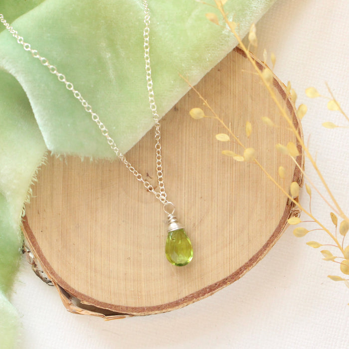 The peridot drop necklace styled on wood with green velvet and dried grass