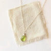 The peridot drop necklace styled on tan linen