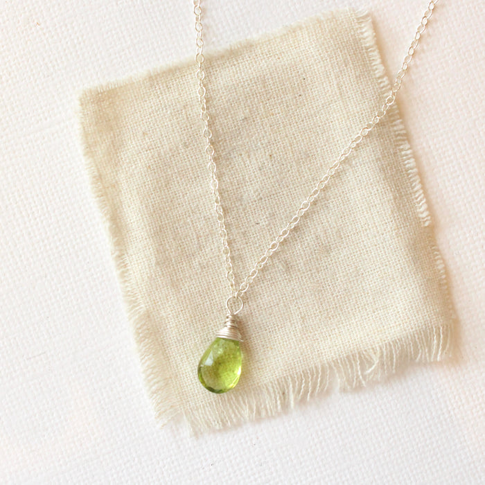 The peridot drop necklace styled on tan linen