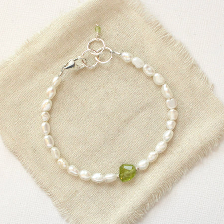 The pearl and peridot bracelet styled on tan linen
