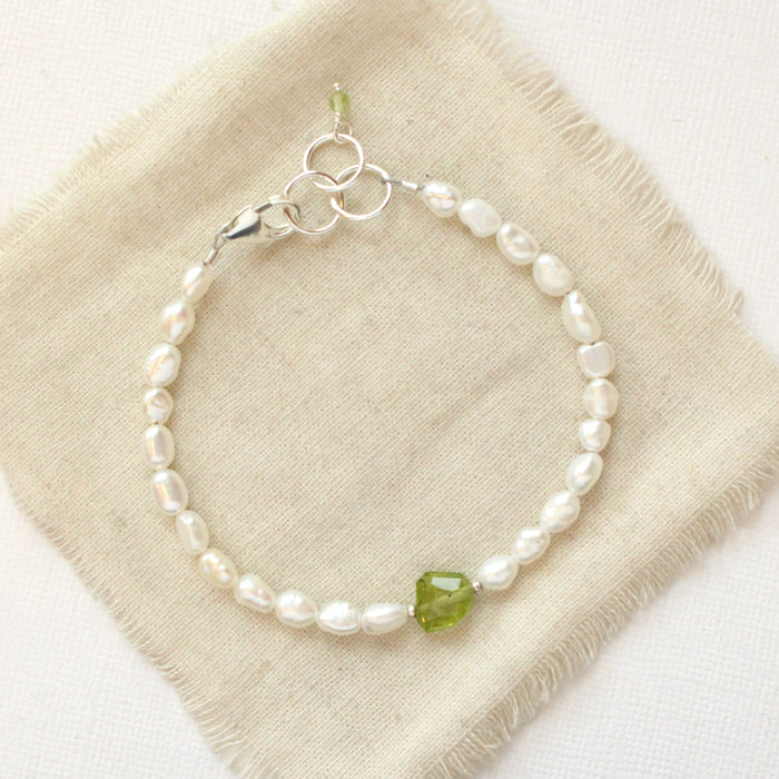 The pearl and peridot bracelet styled on tan linen
