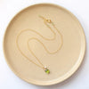 The peridot and pearl gold charm necklace styled on a tan plate to show the adjustable lobster clasp closure