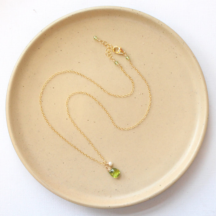 The peridot and pearl gold charm necklace styled on a tan plate to show the adjustable lobster clasp closure