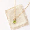 The peridot and pearl charm necklace styled on tan linen
