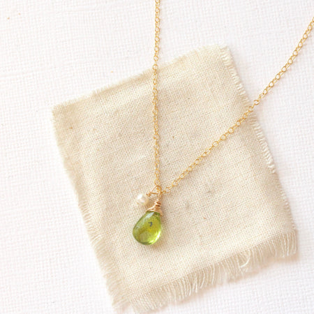 The peridot and pearl charm necklace styled on tan linen
