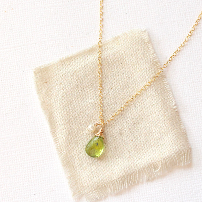 The peridot and pearl charm necklace styled on tan linen