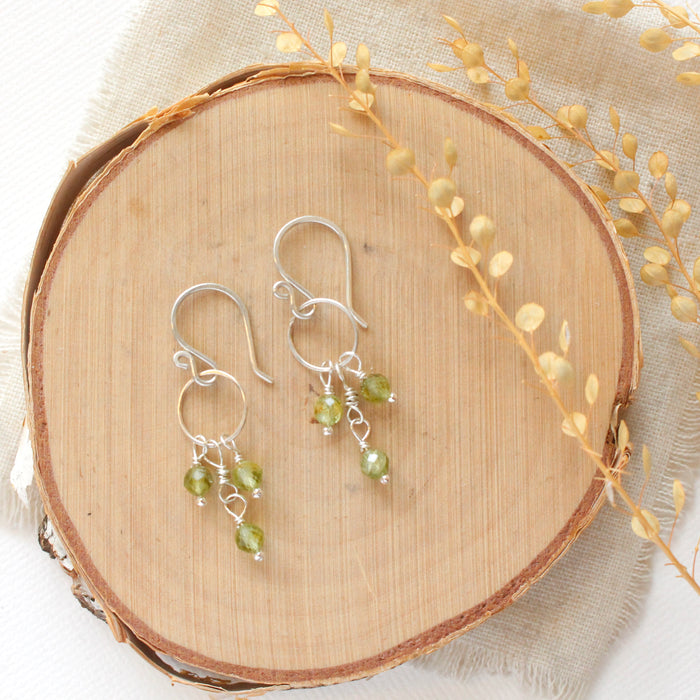 The peridot trio hoop earrings styled on wood with dried grass