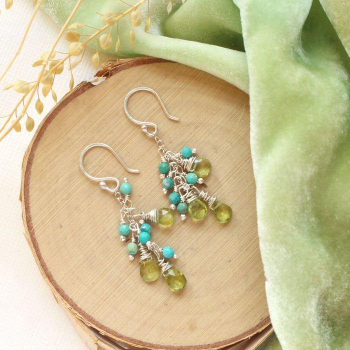 The turquoise & peridot fringe earrings styled on wood with green velvet and dried grass