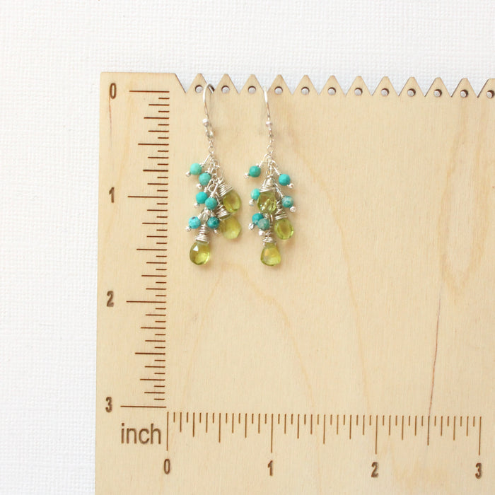 The peridot and turquoise fringe earrings on a wooden ruler for size reference
