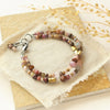 The pink and brass double strand bracelet styled on a tan rock with dried grass