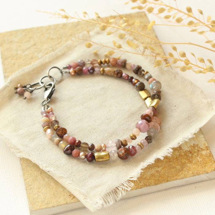 The pink and brass double strand bracelet styled on a tan rock with dried grass
