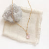 The morganite drop necklace styled on a tan linen with a gray crystal