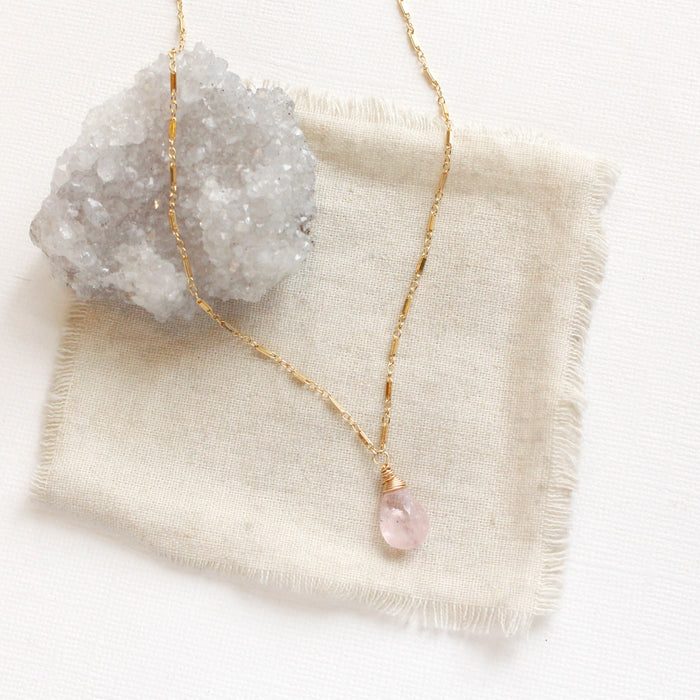 The morganite drop necklace styled on a tan linen with a gray crystal