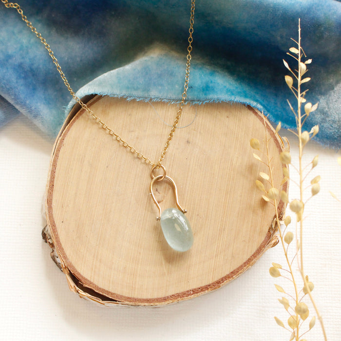 The aquamarine pinned gold necklace styled on wood with blue velvet and dried grass